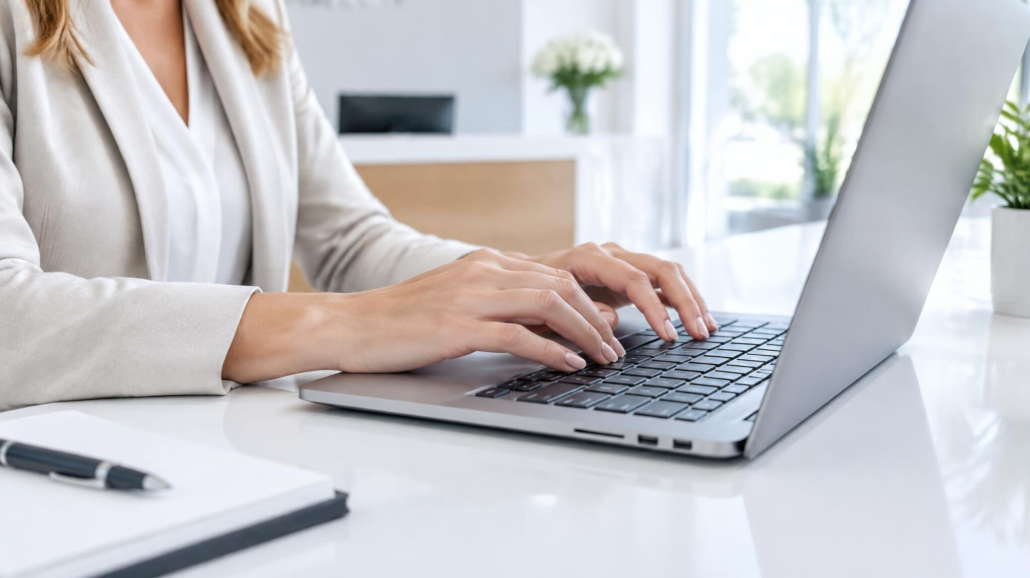 Person typing on a laptop at a bright reception-style desk